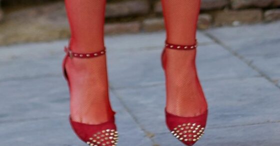 Piernas con medias de rejilla y zapatos rojos de tachuelas, en el aire sobre un suelo de piedra