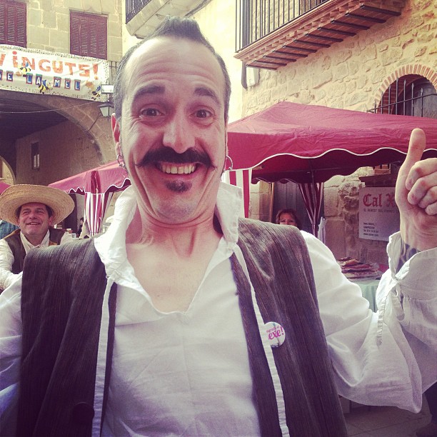 Tamborilero de Arnes con bigote y camisa blanca, con el pulgar arriba y una chapa de M'agrada el sexe!