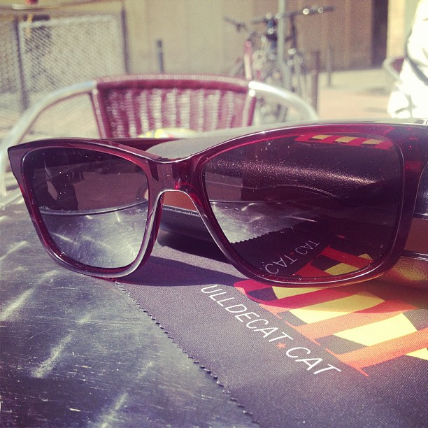 Gafas de sol color vino sobre una mesa de terraza, con el paño de Ull de Cat