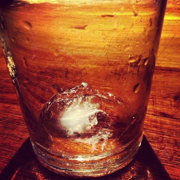 Vaso de cristal con un cubito de hielo sobre una barra de madera
