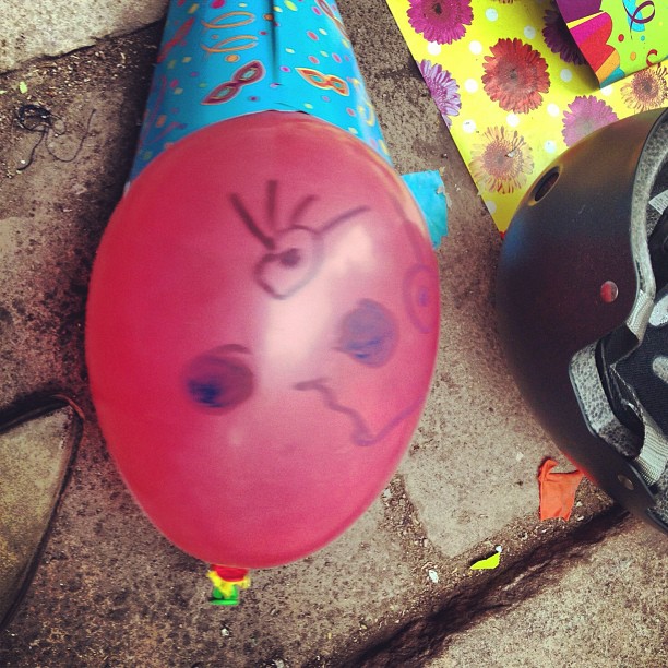 Globo rosa con una cara dibujada, gorro de fiesta y casco en el suelo