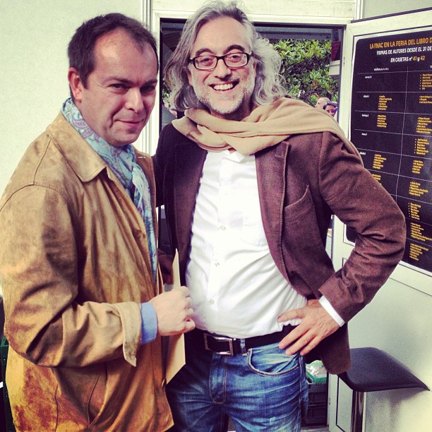 Víctor Amela y Javier Sierra con bufandas junto a una caseta de la Feria del Libro