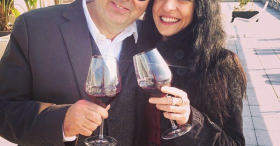 Roser Amills y Oscar Iniesta, con gafas redondas, brindan con copas de vino en una terraza