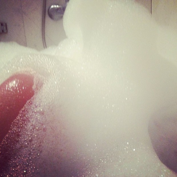 Espuma de baño y la punta de un dedo con la uña pintada de rojo