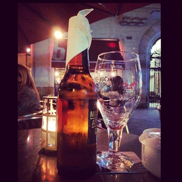 Botella de cerveza vestida con una servilleta, junto a una copa, en una terraza