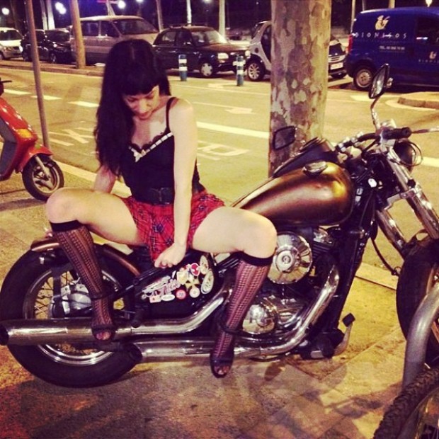 Roser Amills, con corpiño negro, falda de cuadros rojos y medias de rejilla, sentada sobre una moto custom en la calle