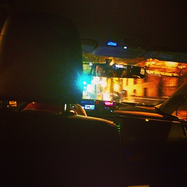 Vista nocturna desde el asiento trasero de un taxi, con el taxímetro iluminado y luces de la calle al fondo