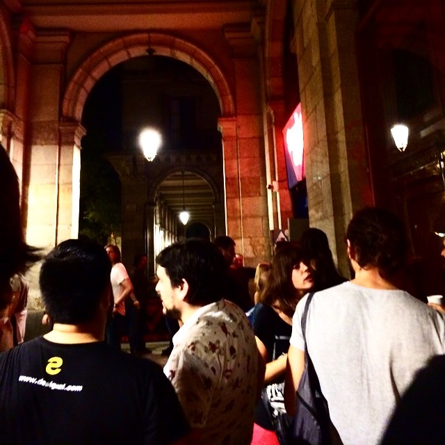 Cola de gente de noche bajo unos soportales de piedra con farolas encendidas