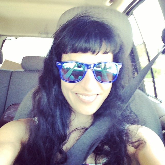 Roser Amills, sonriente, con gafas de sol azules y el cinturón de seguridad puesto, en el asiento de un coche