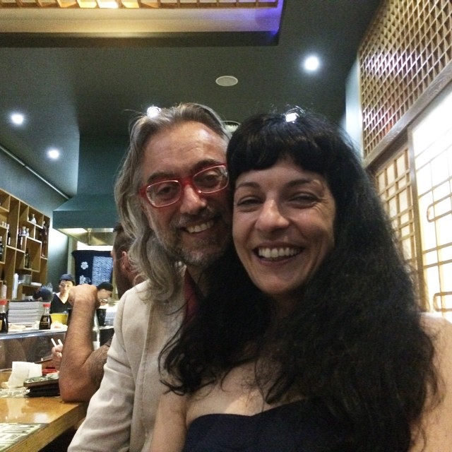 Víctor Amela, de melena gris y gafas rojas, y Roser Amills, de melena negra, sonríen juntos en un restaurante japonés
