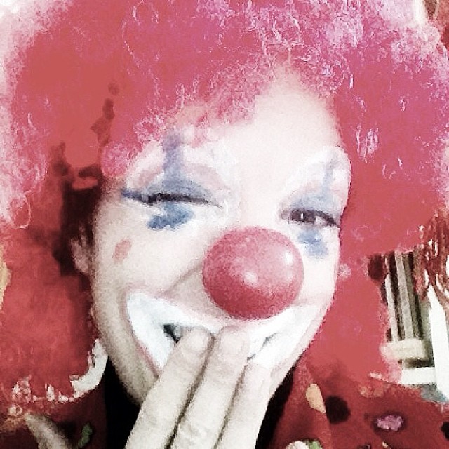 Roser Amills disfrazada de payaso, con peluca roja rizada, nariz roja y la cara pintada de blanco, ríe tapándose la boca con la mano