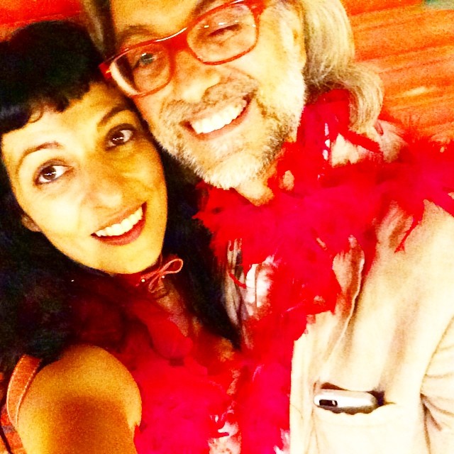 Selfi de una mujer y un hombre con gafas rojas, sonrientes, con una boa de plumas rojas