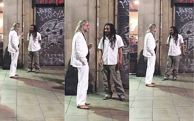 Secuencia de Víctor Amela de blanco hablando con un músico callejero en una calle de Barcelona