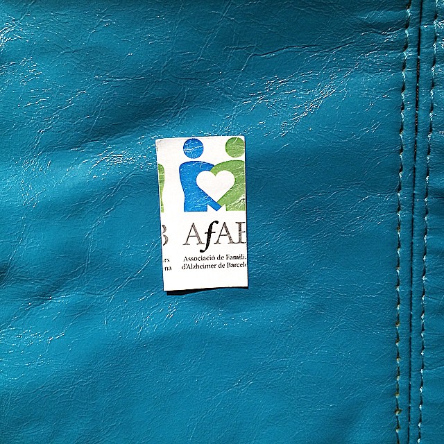 Pin de la Associació de Familiars d'Alzheimer de Barcelona sobre un bolso de cuero azul turquesa