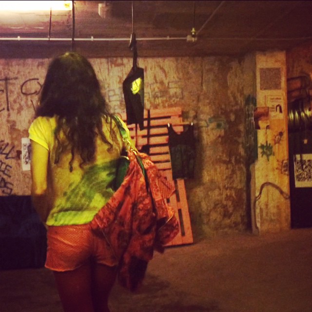 Roser Amills de espaldas en un pasadizo subterráneo con grafitis, con un short naranja, una camiseta amarilla y una bolsa roja a la espalda