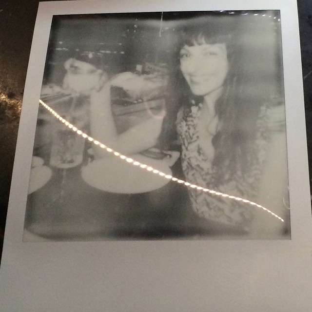 Polaroid en blanco y negro de dos mujeres sentadas ante una mesa, una de ellas sonriendo a cámara