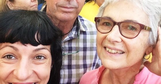 Selfi de Roser Amills somrient amb un home i una dona de cabells grisos, amb roba groga al fons