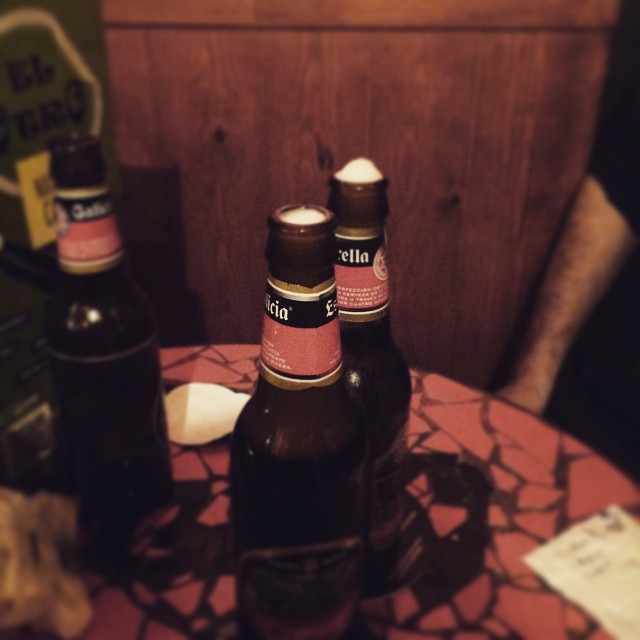 Tres botellines de cerveza sobre una mesa con mantel rojo, en la penumbra de un bar