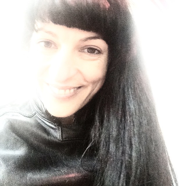 Roser Amills sonriendo, con el pelo largo y flequillo, con chaqueta negra y un fuerte reflejo de luz