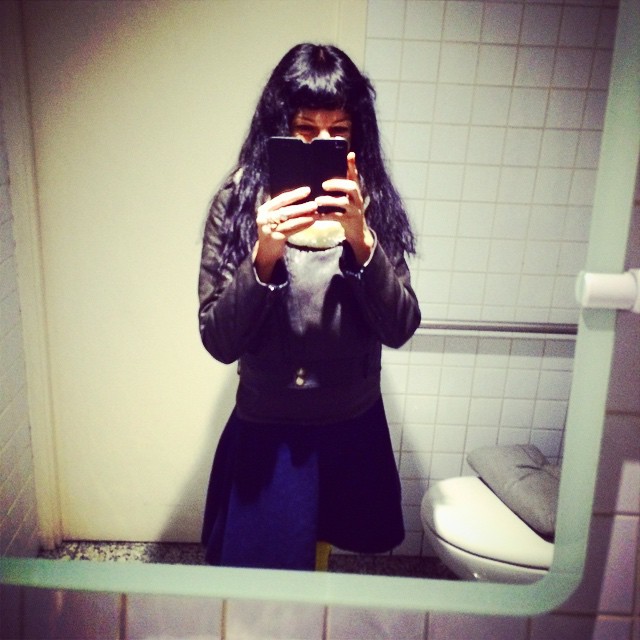 Roser Amills, con cazadora de cuero negra y falda azul, fotografiándose con el móvil en el espejo de un lavabo