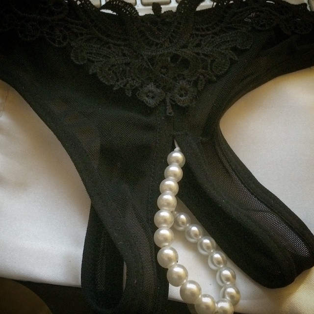 Braguitas negras de encaje con un collar de perlas sobre una tela blanca