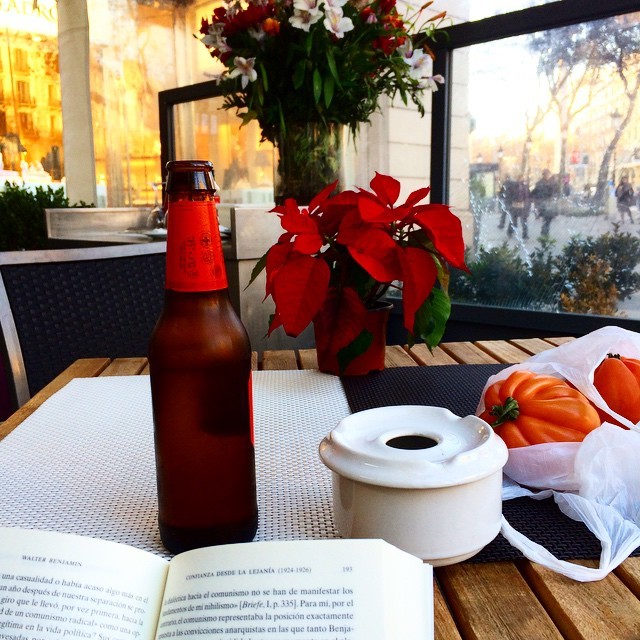 Cerveza, flores de Pascua rojas, un cenicero y un libro abierto sobre la mesa de una terraza