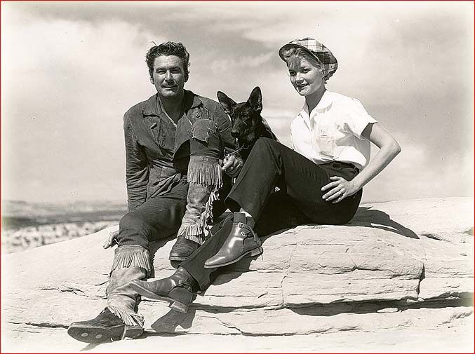 Errol Flynn y Patrice Wymore sentados en unas rocas junto a un perro, en blanco y negro