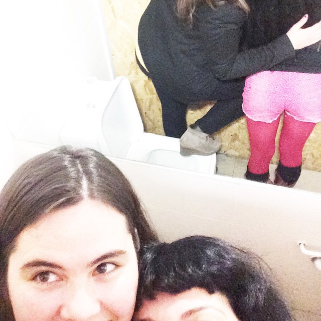 Autoretrat de Joana Abrines i Roser Amills, cara a cara, al lavabo, amb el reflex de les cames amb mitges roses a l’espill