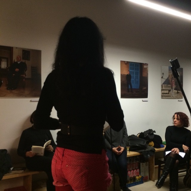 Roser Amills, d’esquena, amb jersei negre i pantalons vermells, recita davant el públic assegut a l’Espai Mallorca