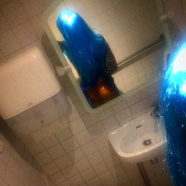 Roser Amills con peluca azul fotografiada desde arriba en un lavabo público, serie Amills Public WC