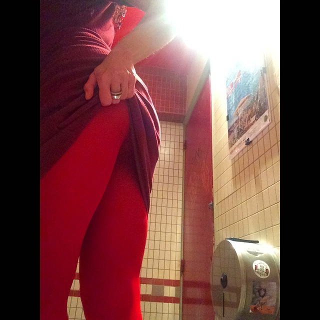 Roser Amills con vestido y medias rojas levantándose la falda en el lavabo de azulejos de El Otro bar, serie Amills Public WC