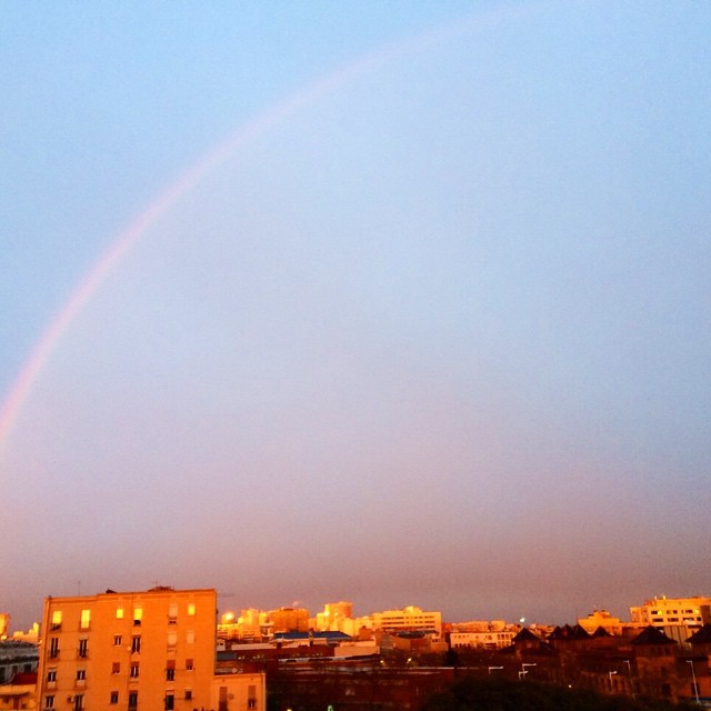 Arco iris sobre el cielo azul y los edificios iluminados por el atardecer en Barcelona