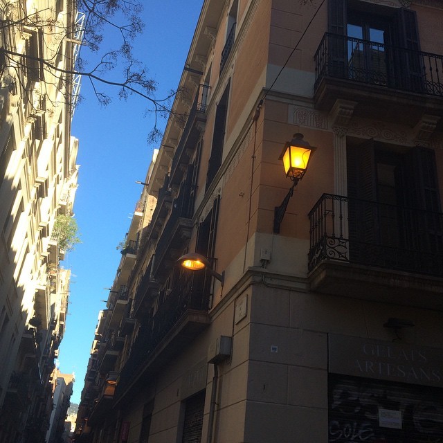 Farol encendido en la fachada de una calle estrecha de Barcelona bajo el cielo azul de la mañana