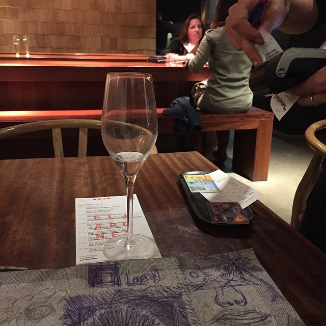 Copa de cava y un mantel de papel con dibujos sobre una mesa de madera, en una galería