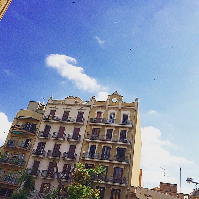 Fachada de un edificio modernista con balcones bajo un cielo azul con nubes