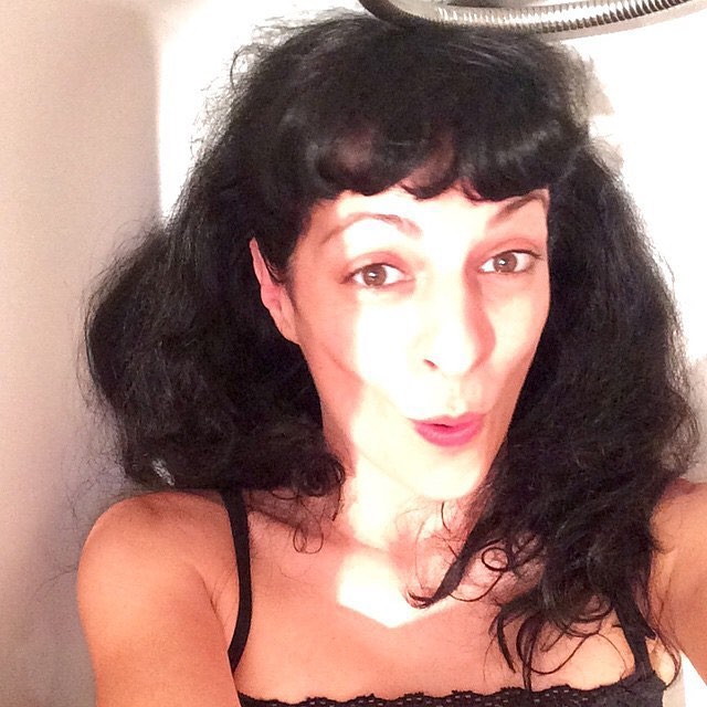 Roser Amills con flequillo y el pelo oscuro revuelto, lanzando un beso a la cámara bajo una alcachofa de ducha