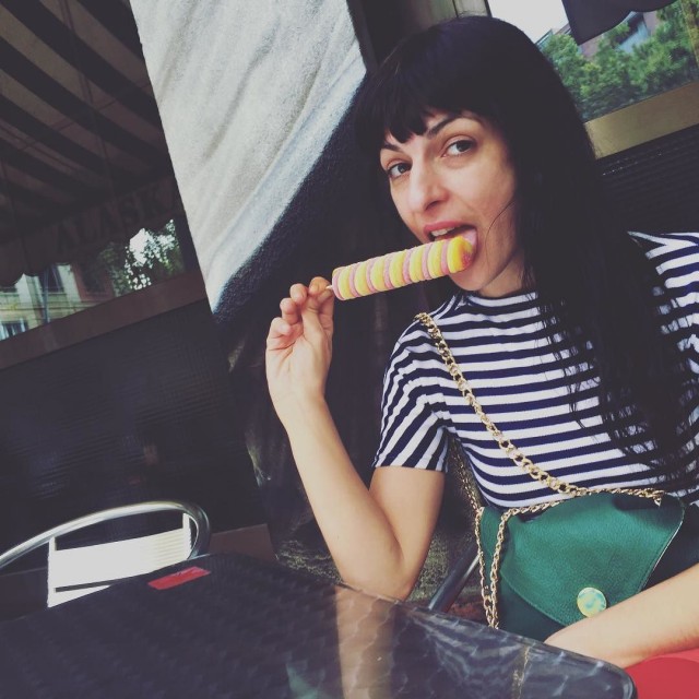 Roser Amills con camiseta de rayas y bolso verde, lamiendo un helado de colores en la terraza de un bar