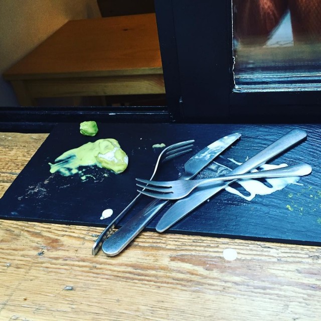 Cubiertos y restos de crema verde sobre una pizarra, junto a una ventana