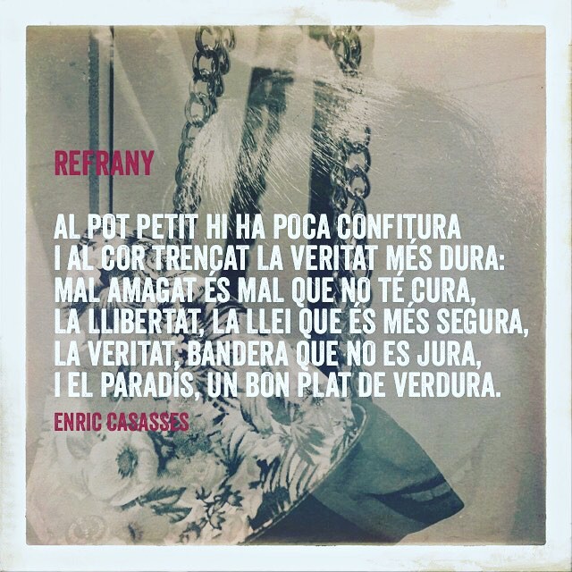 Poema «Refrany» d’Enric Casasses, en lletres blanques sobre una fotografia d’una bossa de flors amb cadenes: «Al pot petit hi ha poca confitura i al cor trencat la veritat més dura…»