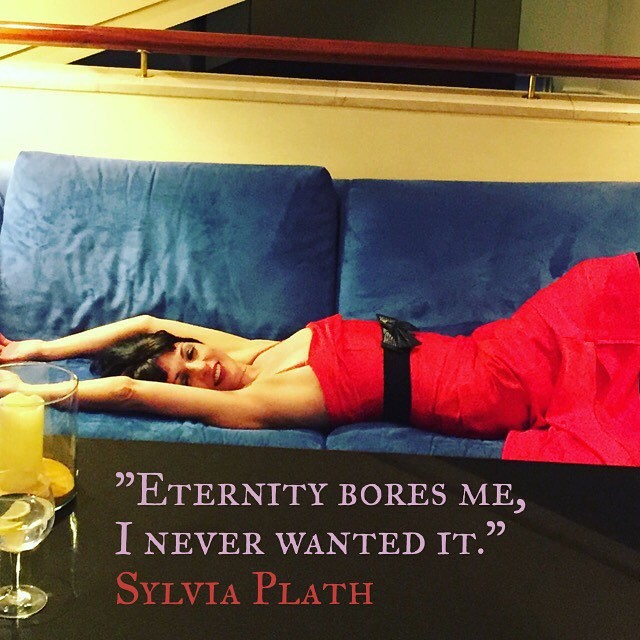 Roser Amills tumbada en un sofá azul con vestido rojo, con la cita de Sylvia Plath: Eternity bores me, I never wanted it