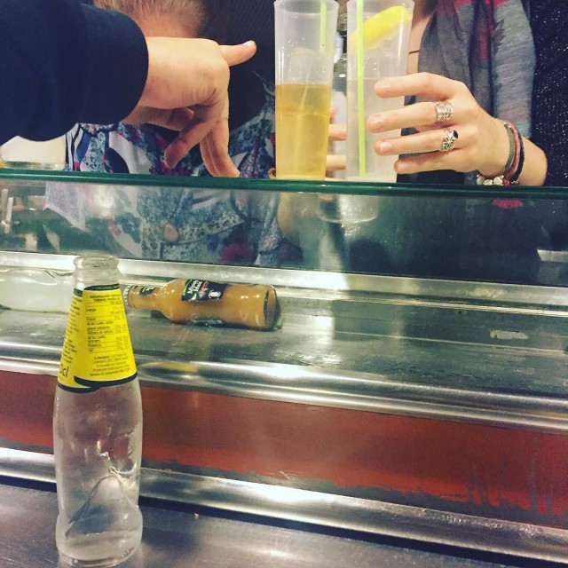Barra de bar con una botella de zumo tumbada, una botella de tónica vacía, dos vasos con limón y una mano señalando hacia abajo