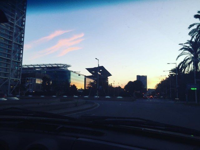 Atardecer visto desde el coche: cielo con nubes rosadas sobre edificios de Barcelona y palmeras