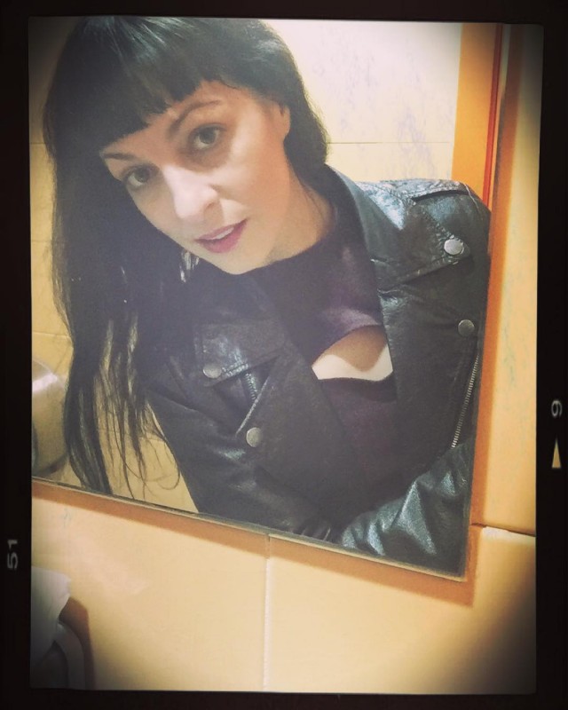 Selfi de Roser Amills en el espejo de un lavabo público, con chaqueta de cuero negra, flequillo y marco de fotografía antigua