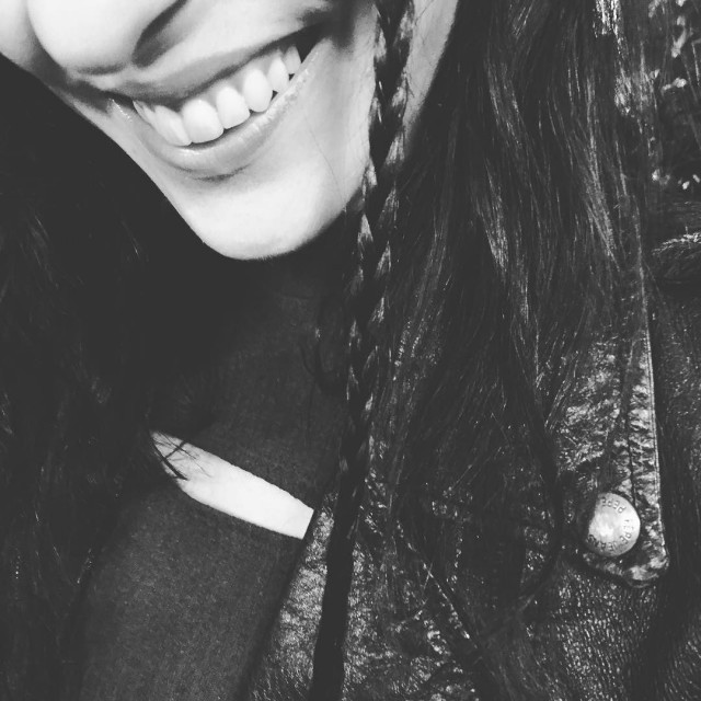 Primer plano en blanco y negro de la sonrisa de Roser Amills, con una trenza en el pelo y una chaqueta de cuero