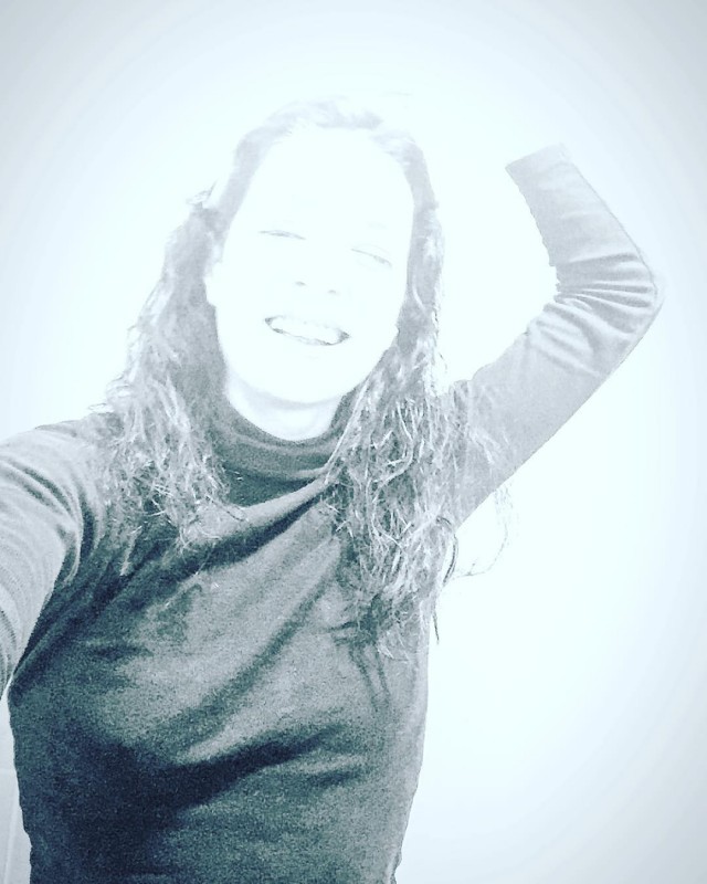 Retrato sonriente de una mujer de pelo largo ondulado con jersey de cuello alto gris y un brazo levantado