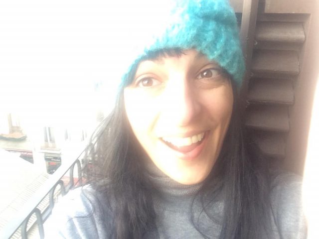 Autorretrato sonriente con un gorro de lana azul turquesa, junto a una barandilla y una escalera