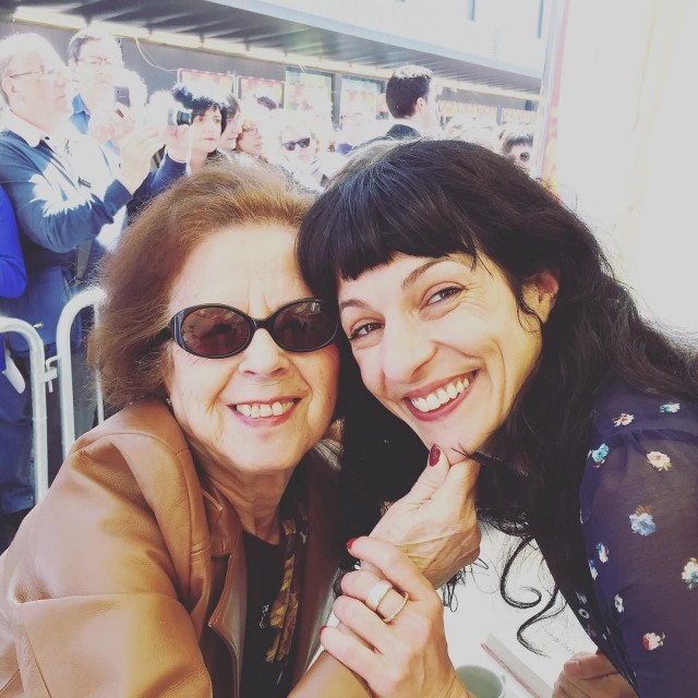 Dos mujeres sonrientes abrazadas, una con gafas de sol, con un público detrás