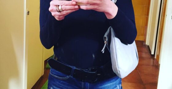 Selfie en el espejo de un lavabo: jersey oscuro, pantalón corto vaquero y bolso blanco