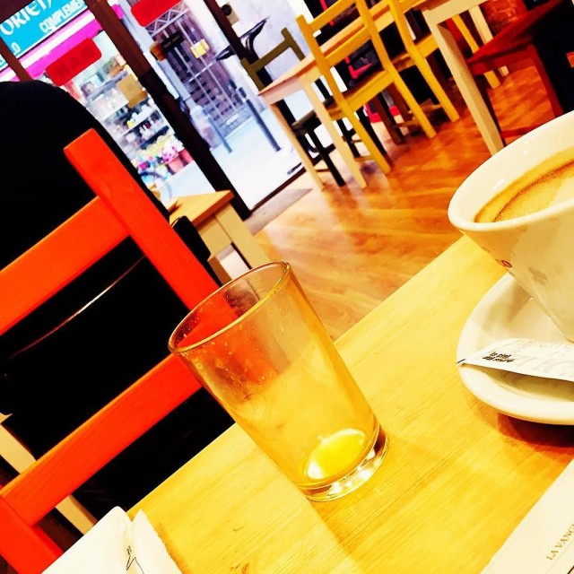 Vaso vacío y taza de café sobre una mesa de madera, con sillas rojas al fondo