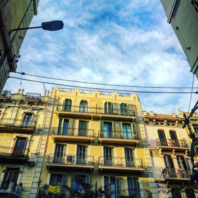 Façana groga d'un edifici amb balcons sota un cel amb núvols